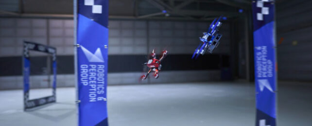 Blue autonomous drone races red human-piloted drone through a square racing gate.