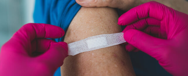 pink gloves holding a bandaid on a patient's arm