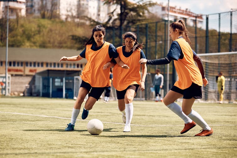 Three young women play football.