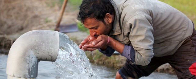 man drinking water from a pipe