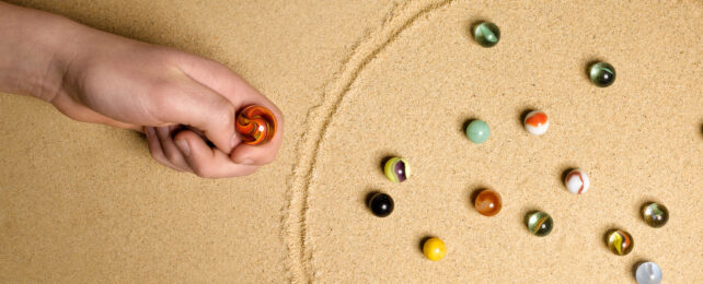 hand holding a marble near a circle with other marbles