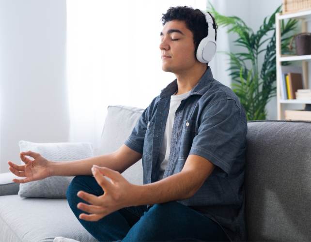 A masculine person meditating on a couch