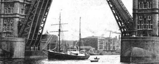 A black and white image of a ship sailing under a bridge