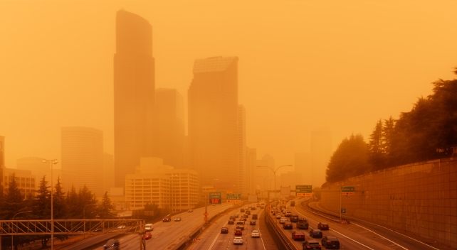 A highway with a city in the background blanketed by thick smoke 